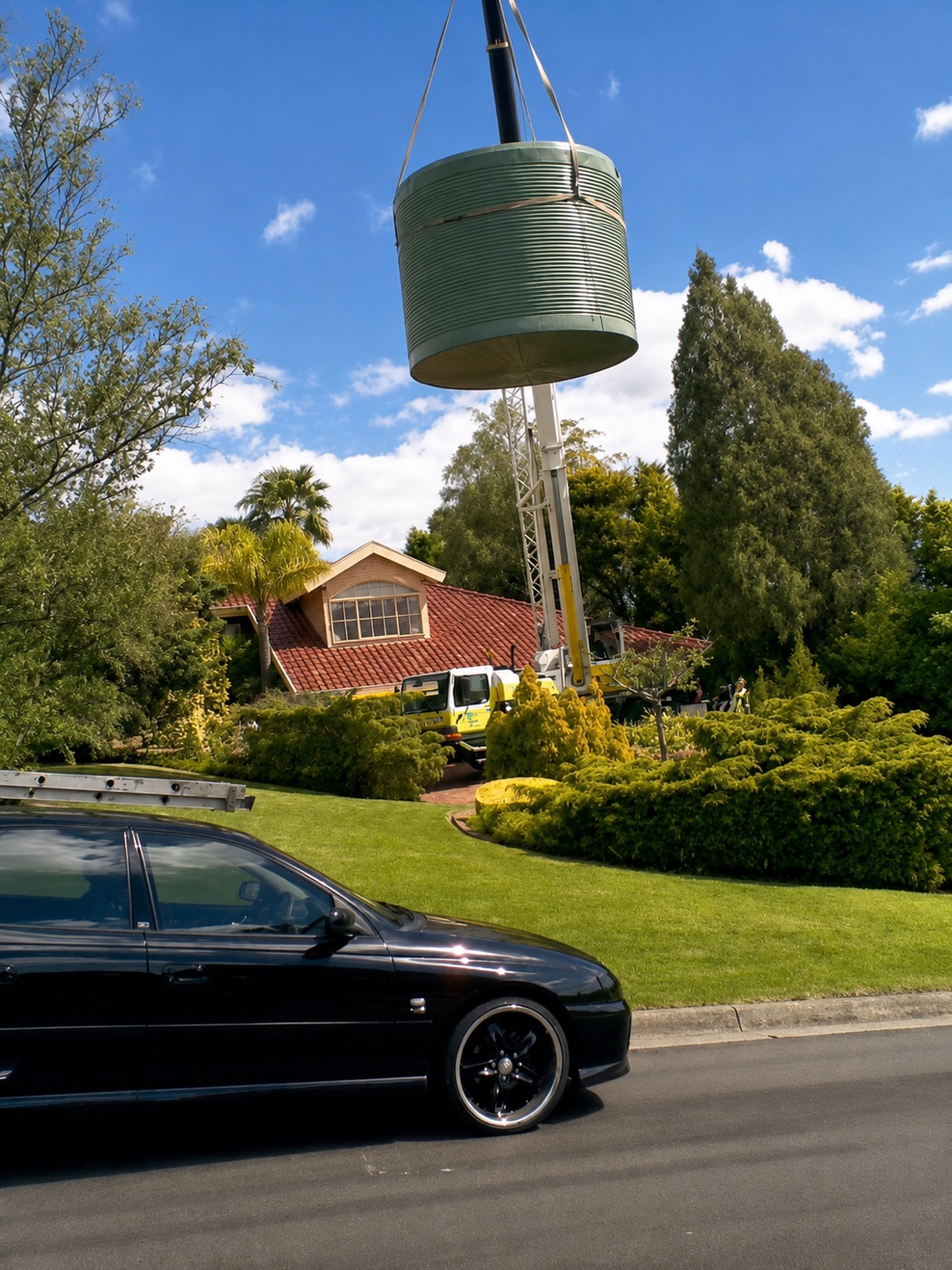 A rainwater tank being craned into a garden by Breeze Plumbing
